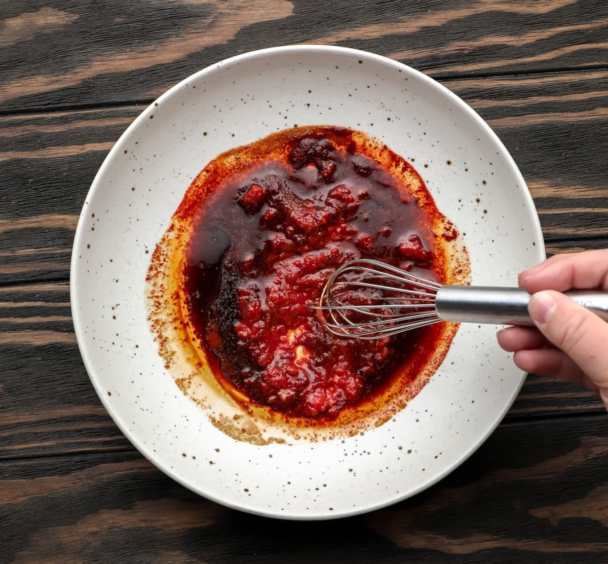 reddish sauce being mixed in a speckled bowl on wood background