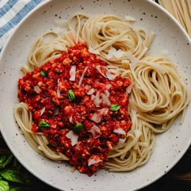 square image of a bowl with lots of noodles and red vegan bolognese on one side of the pasta