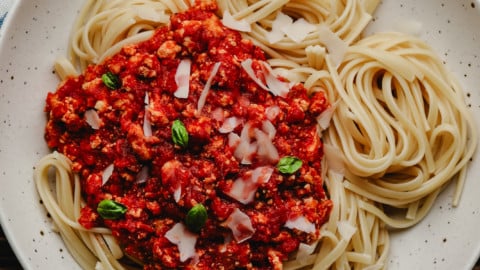 square image of a bowl with lots of noodles and red vegan bolognese on one side of the pasta