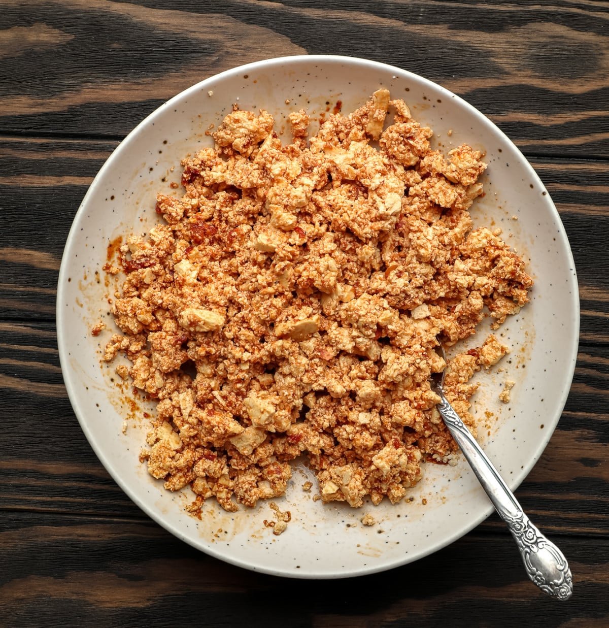 tofu crumbles in a bowl with a spoon, mixed up with a reddish sauce