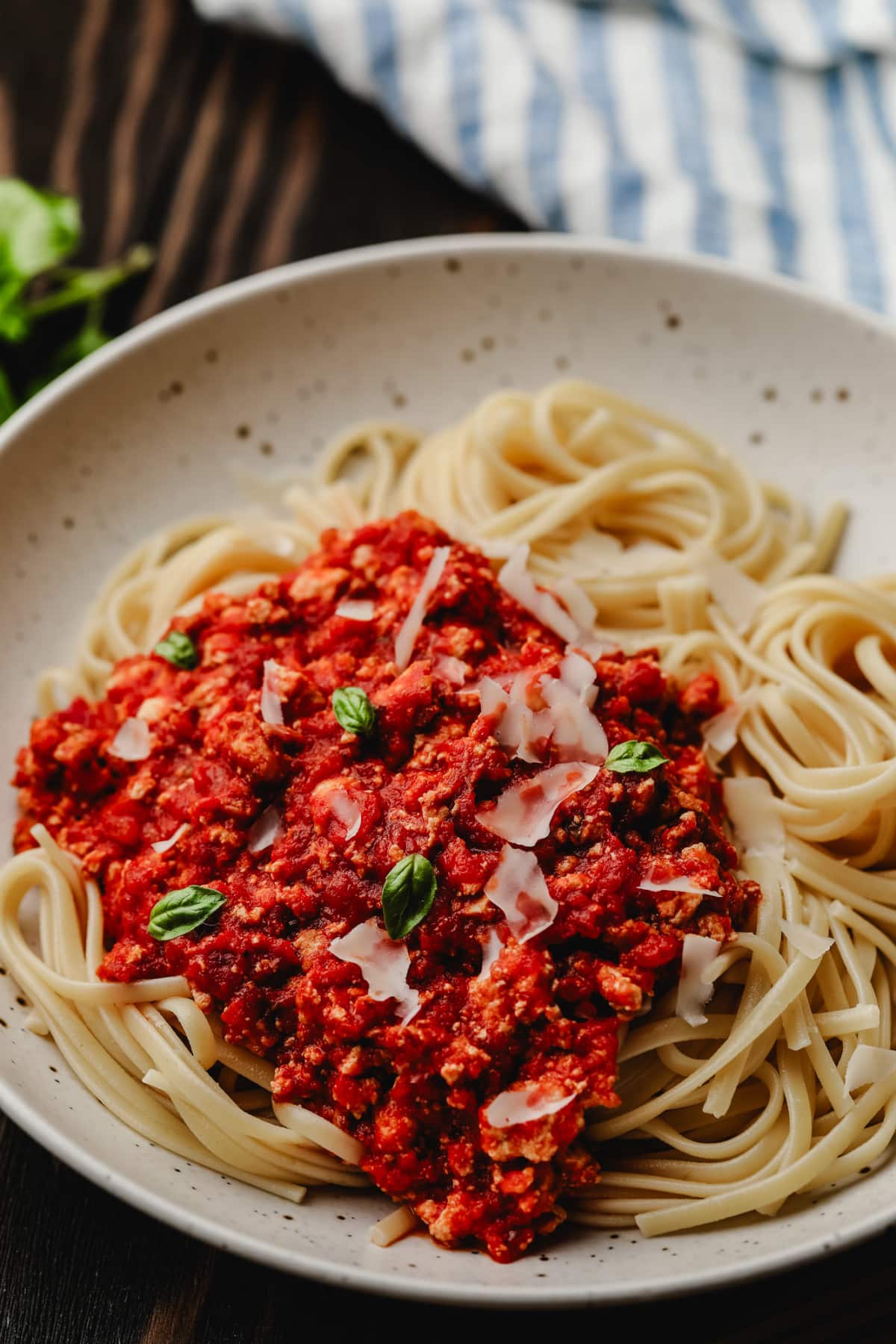 noodles with a vegan bolognese sauce, parmesan and little basil leaves on wood background