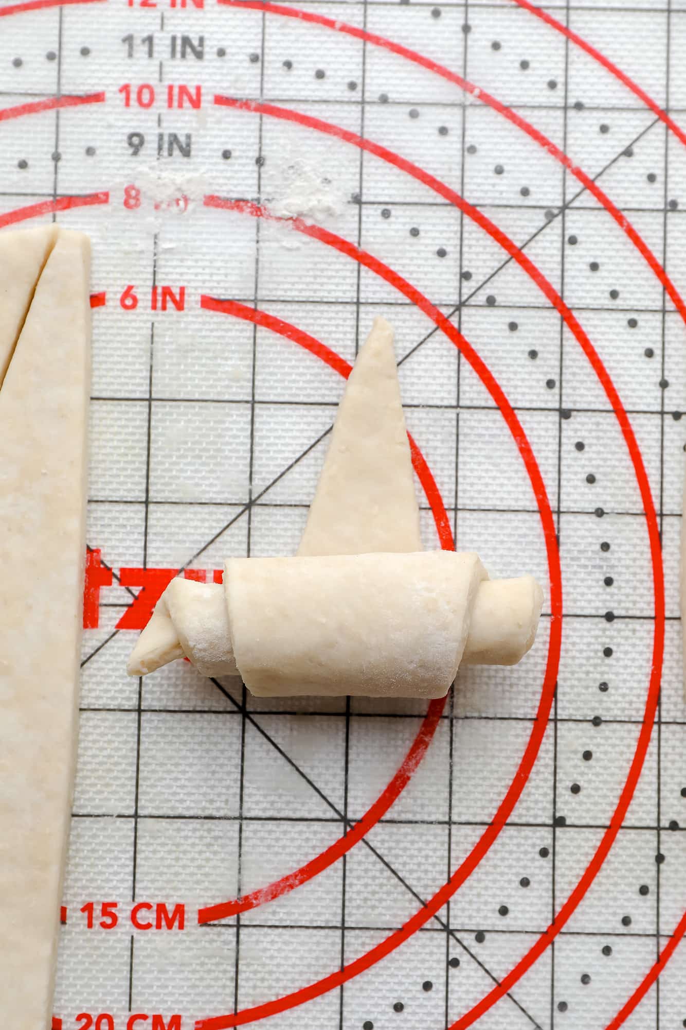 rolling croissant dough into a crescent roll on a pastry mat.