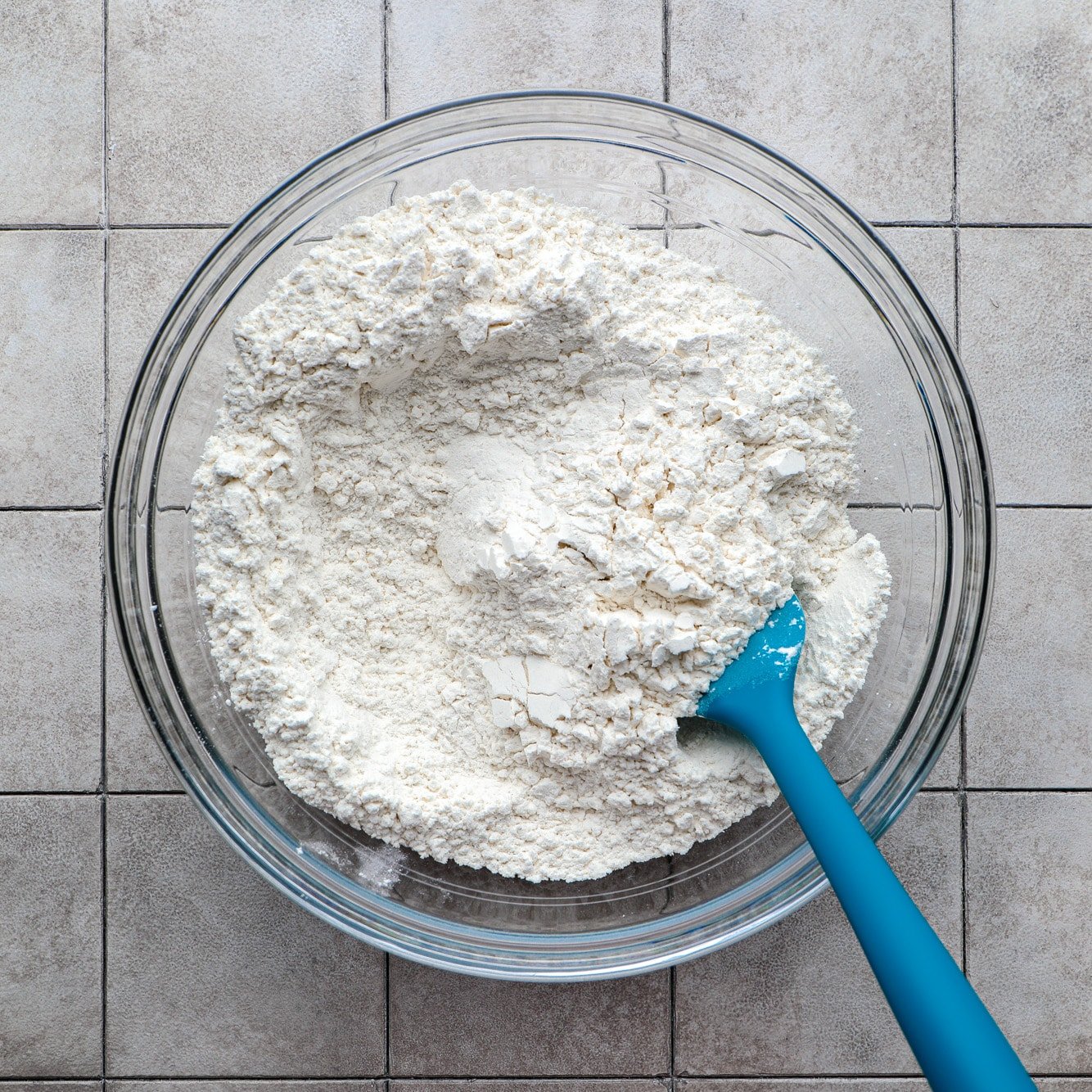 dry ingredients for vegan focaccia in a glass bowl with a blue spatula.