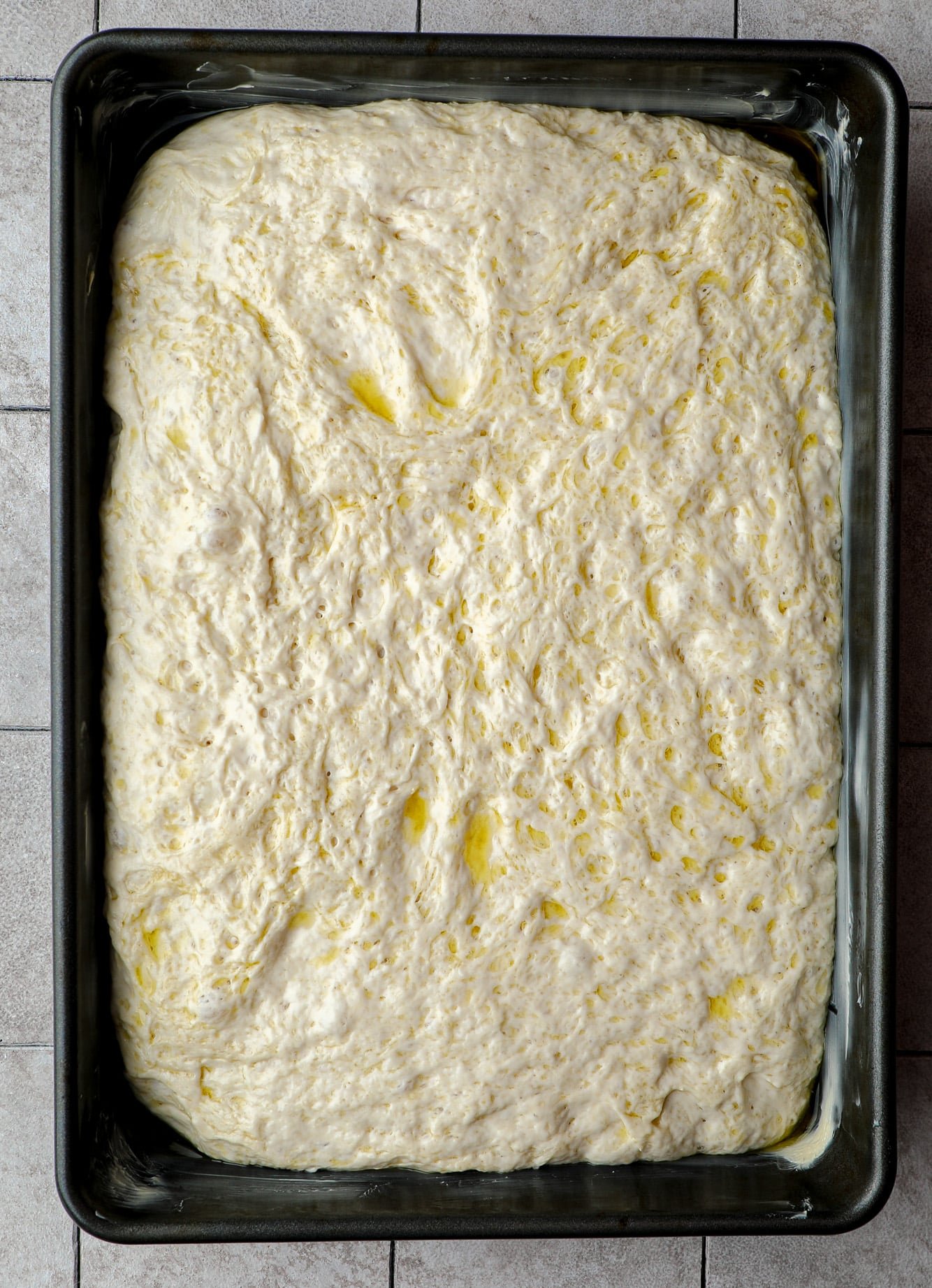 focaccia dough in a large black baking pan.