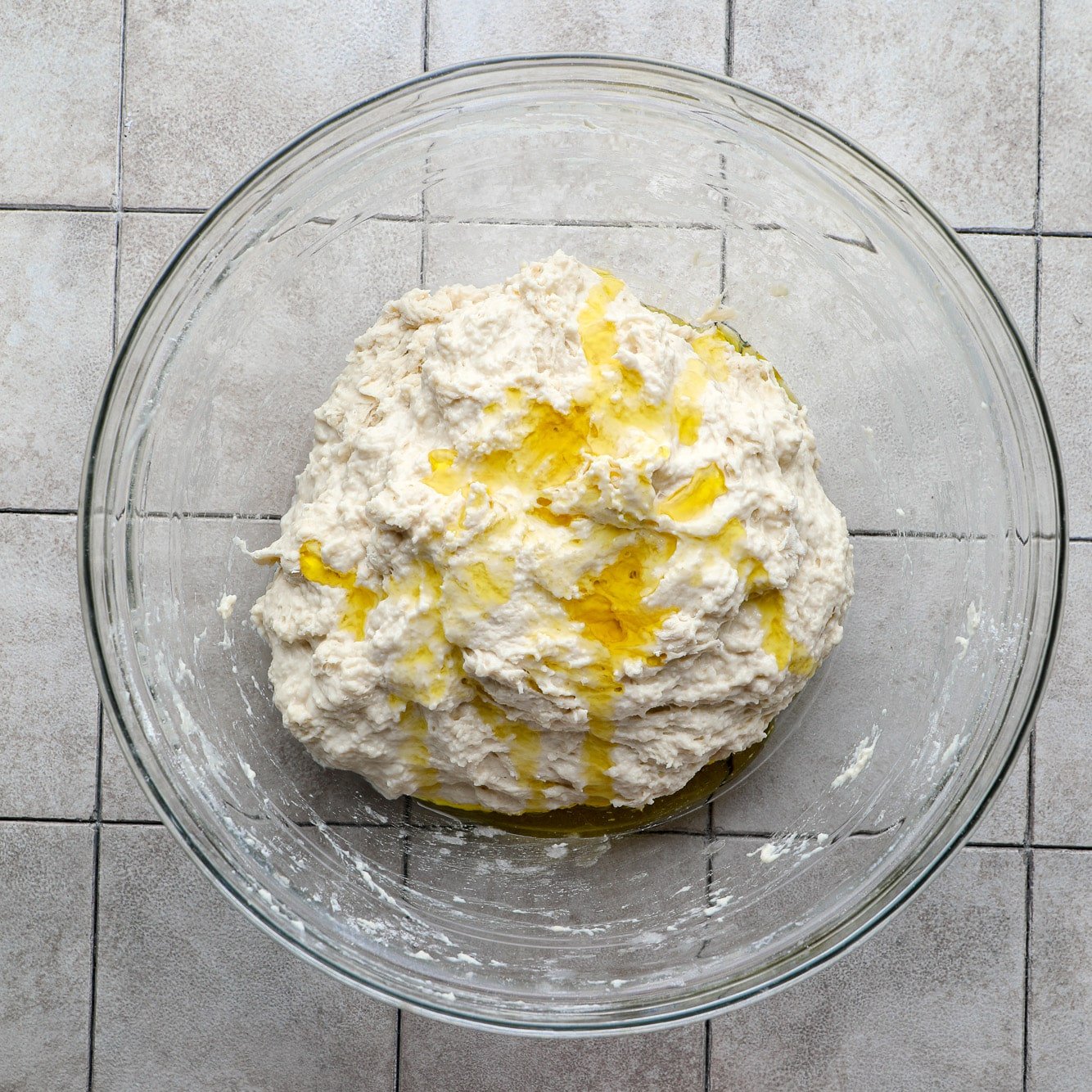 a ball of focaccia dough with oil on top in a glass bowl.