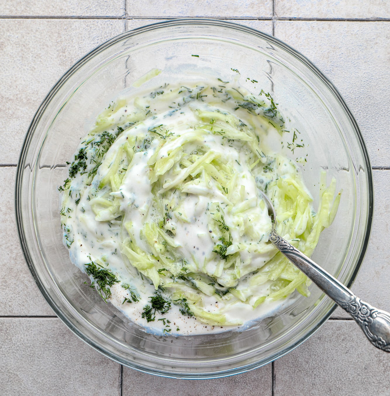 stirring the ingredients for tzatziki sauce in a glass bowl.