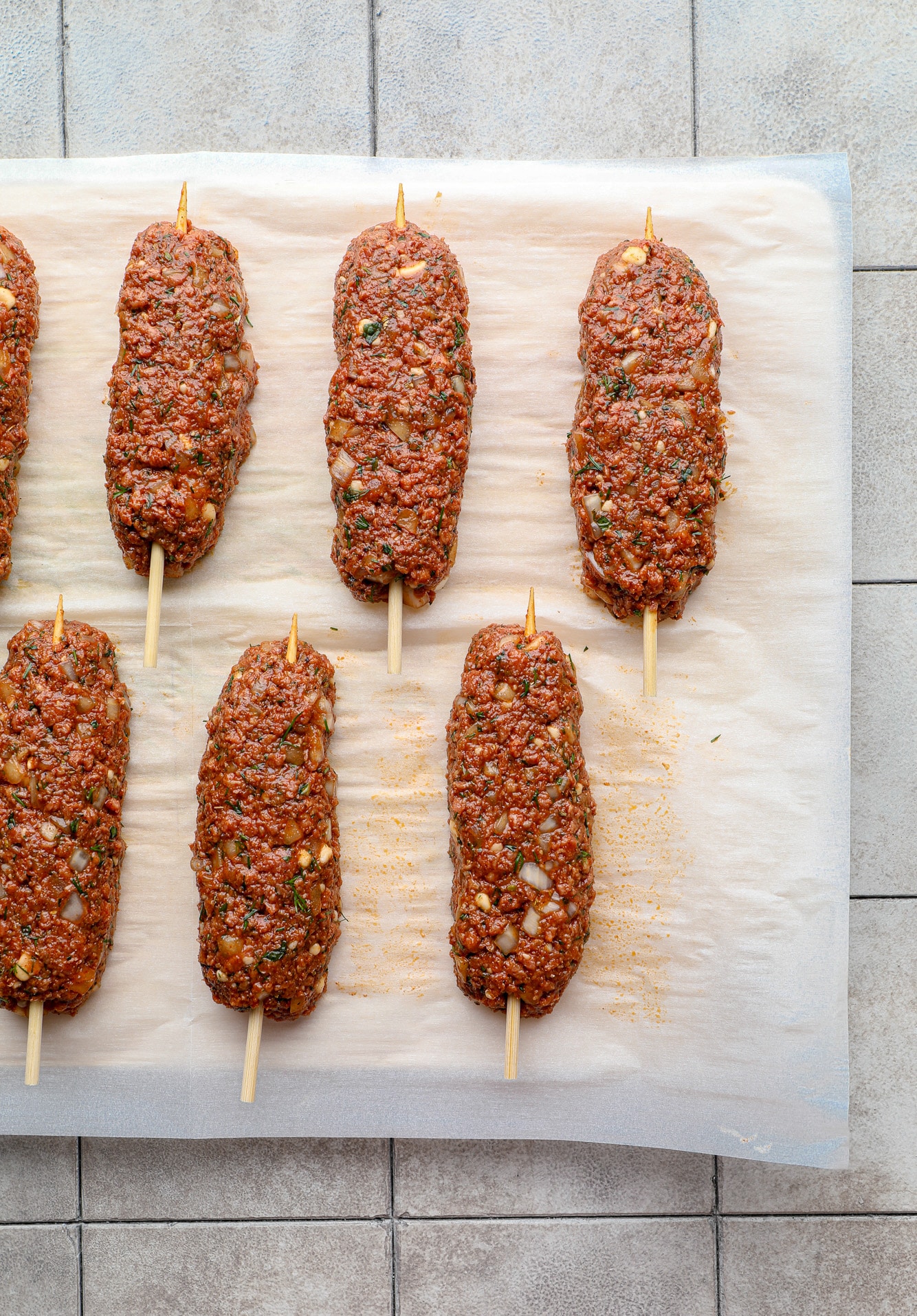 uncooked vegan kofta on wooden skewers on a parchment-lined baking sheet.