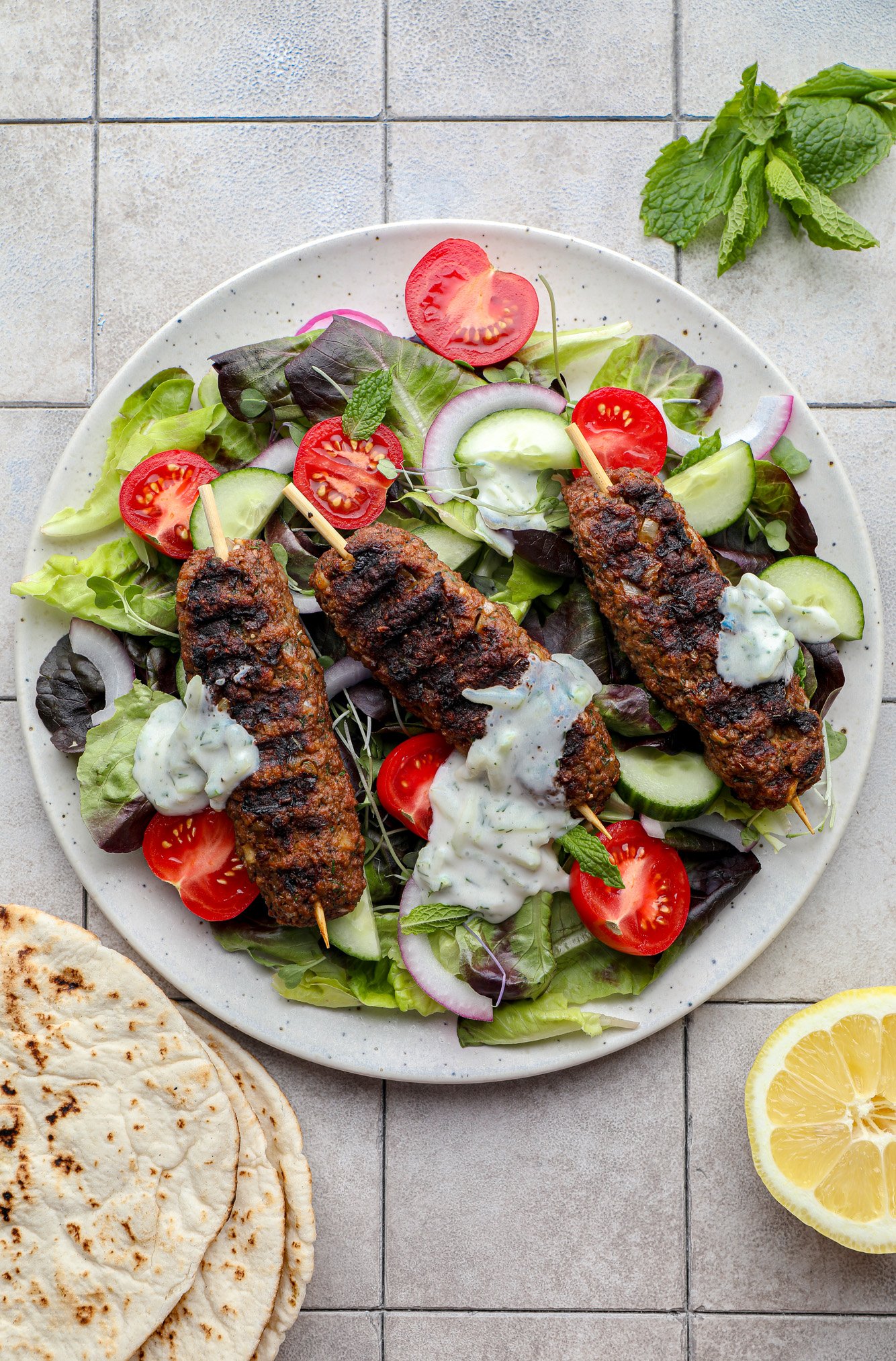 grilled vegan kofta on top of a green salad with vegetables and tzatziki.
