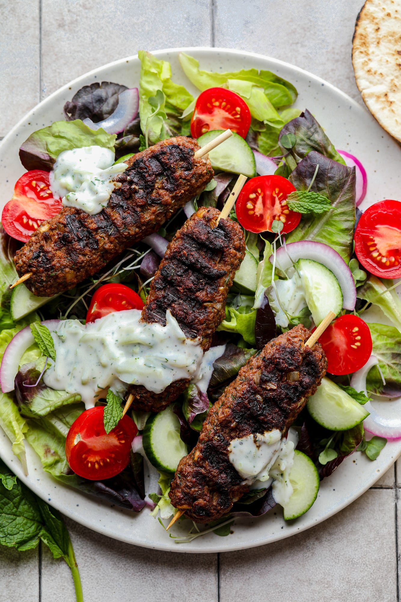 grilled vegan kofta on top of a green salad with vegetables and tzatziki.