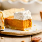 a slice of vegan pumpkin pie with a bite removed and whipped cream on top.