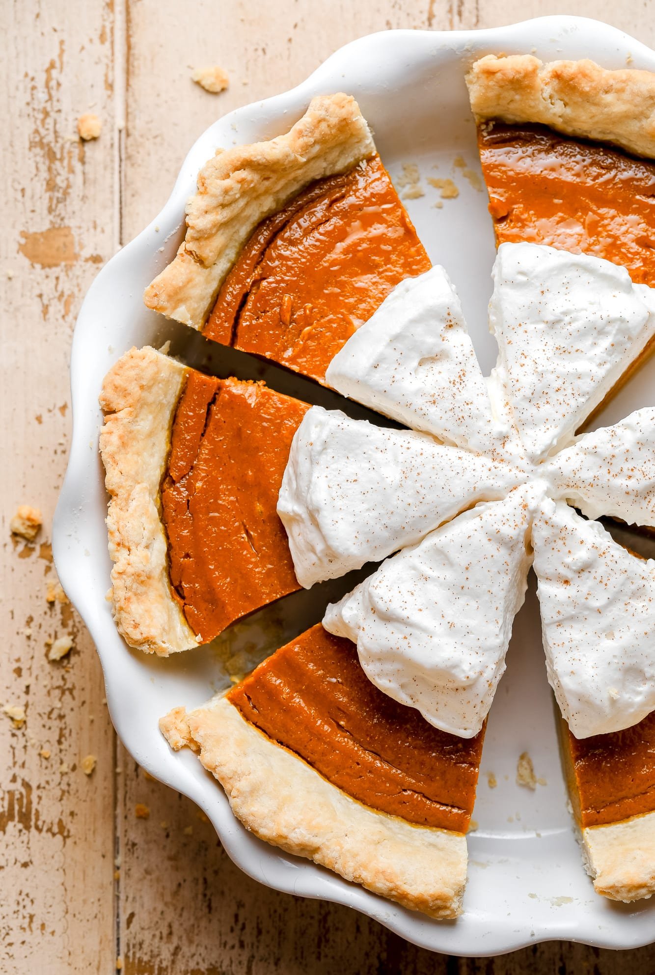close up on sliced vegan pumpkin pie with whipped cream on top in a white pie dish.