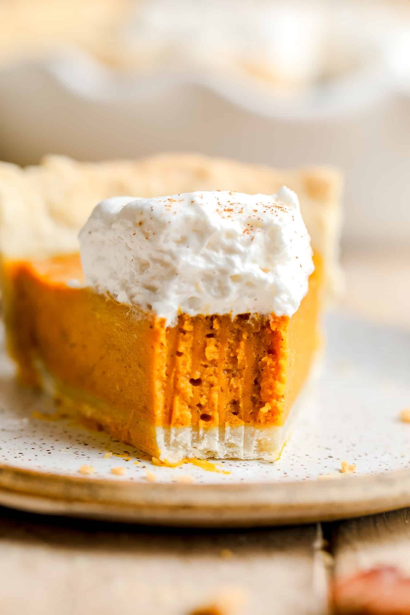 a slice of vegan pumpkin pie with a bite removed and whipped cream on top.