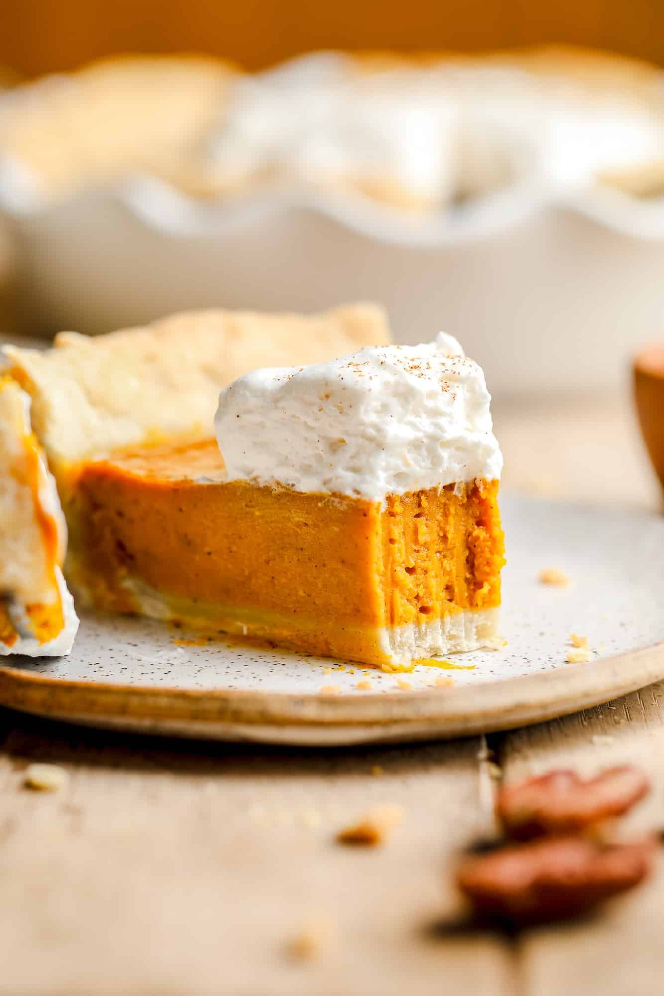 a slice of vegan pumpkin pie with a bite removed and whipped cream on top.