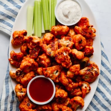 buffalo cauliflower wings, celery sticks, a bowl of ranch dressing, and a bowl of buffalo sauce on a large white platter.