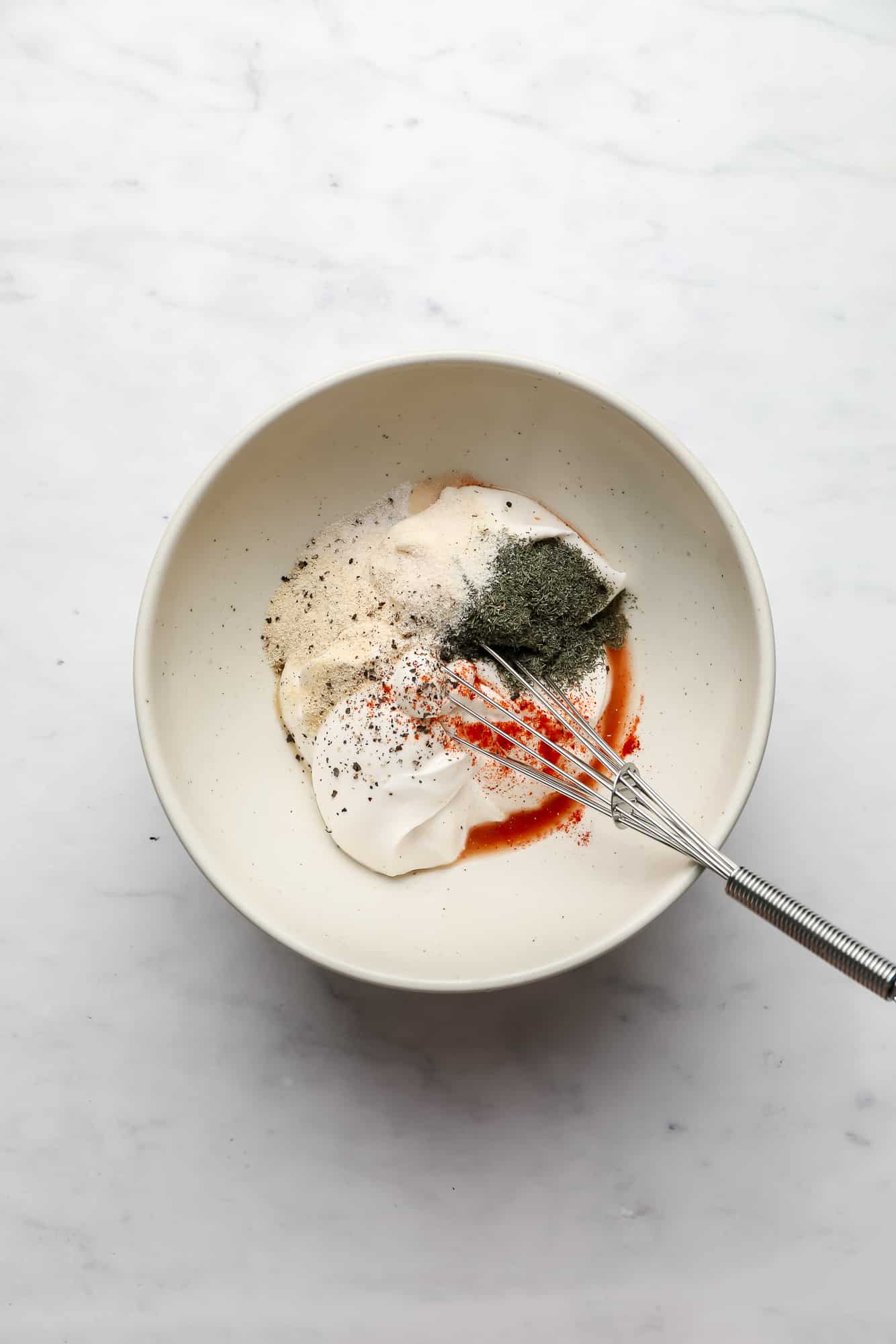 whisking the ingredients for vegan ranch dressing in a white bowl.