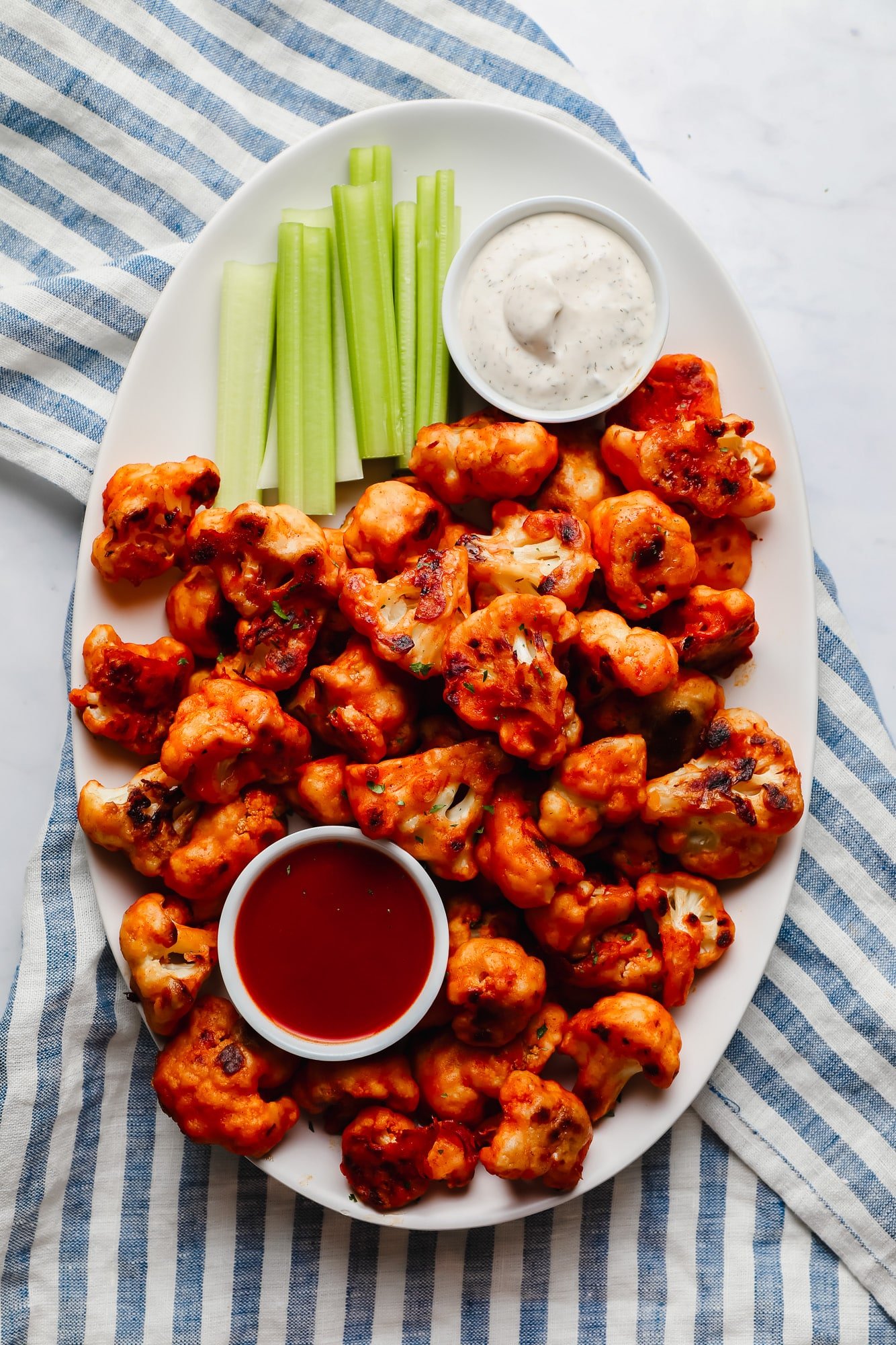buffalo cauliflower wings, celery sticks, a bowl of ranch dressing, and a bowl of buffalo sauce on a large white platter.