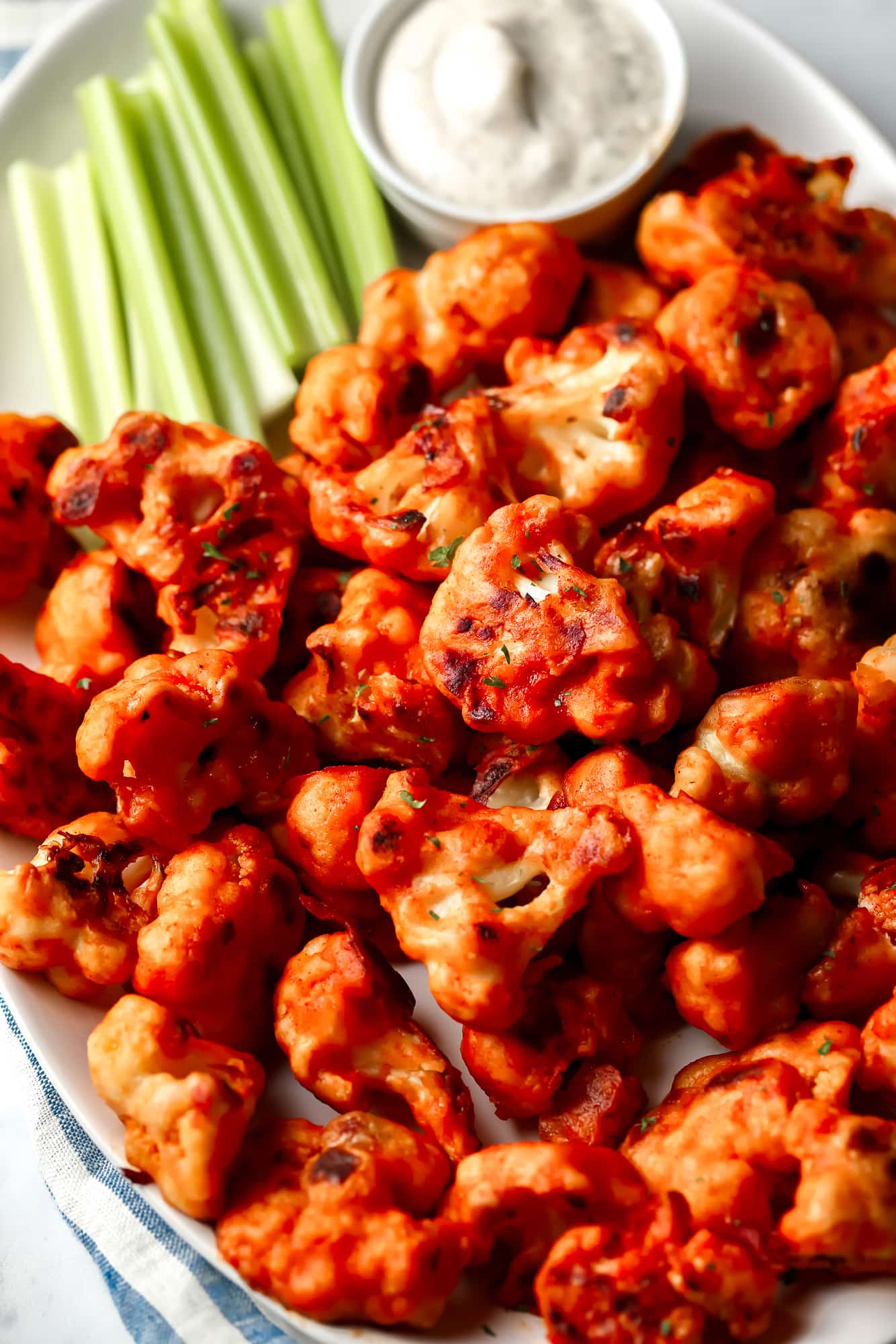 close up on buffalo cauliflower on a white platter with celery sticks and ranch dipping sauce on the side.