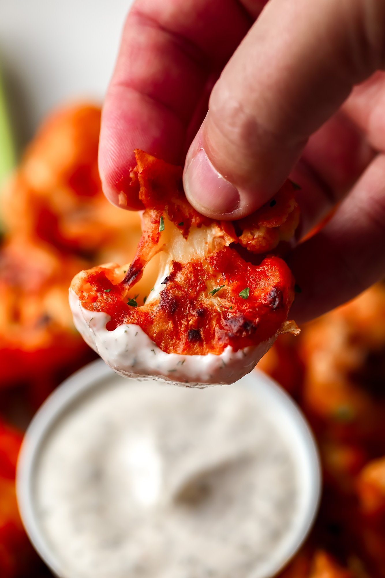 a hand dipping a buffalo cauliflower into vegan ranch dressing.