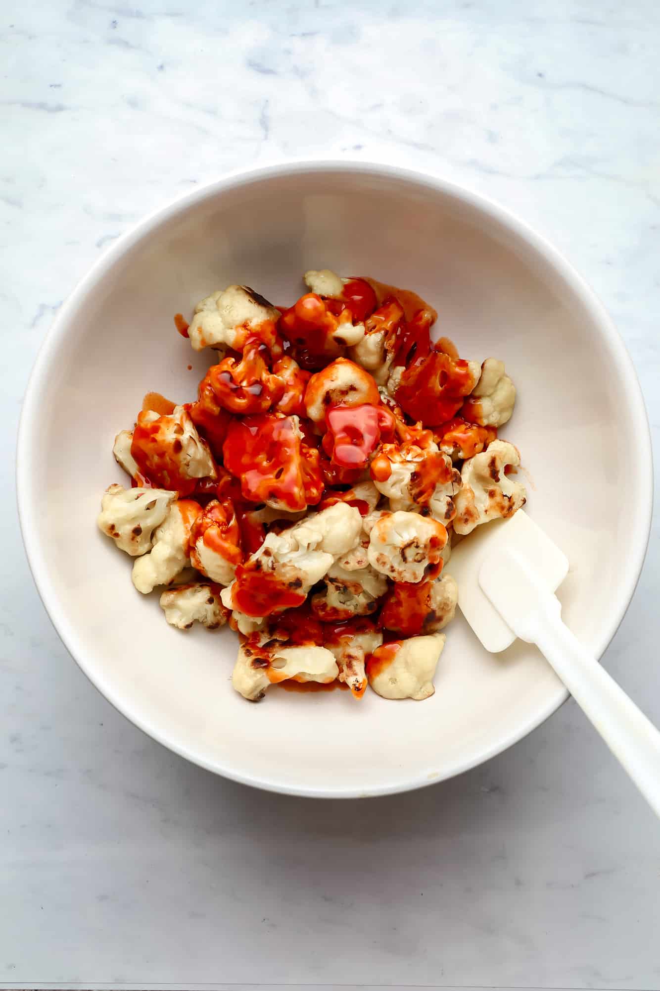 tossing cauliflower wings in buffalo sauce in a white bowl.