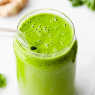 square image of a kale smoothie in a glass with a straw