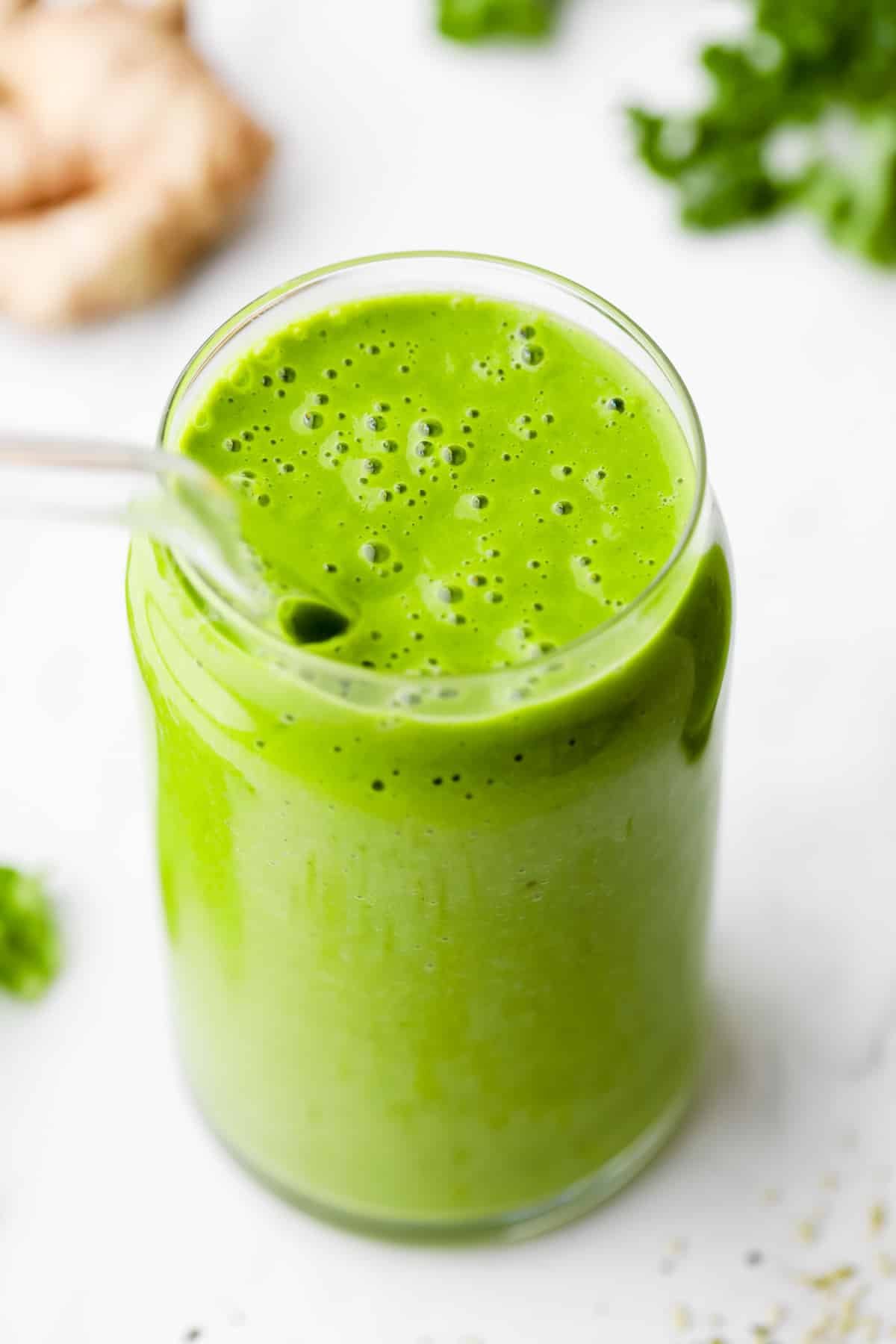 kale smoothie in a glass cup and glass straw, ginger and kale on board