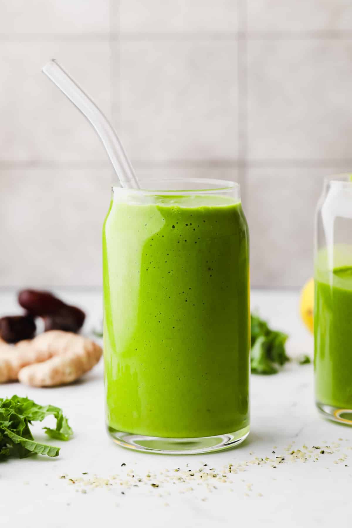 glass cup full of green smoothie with glass straw, grey background