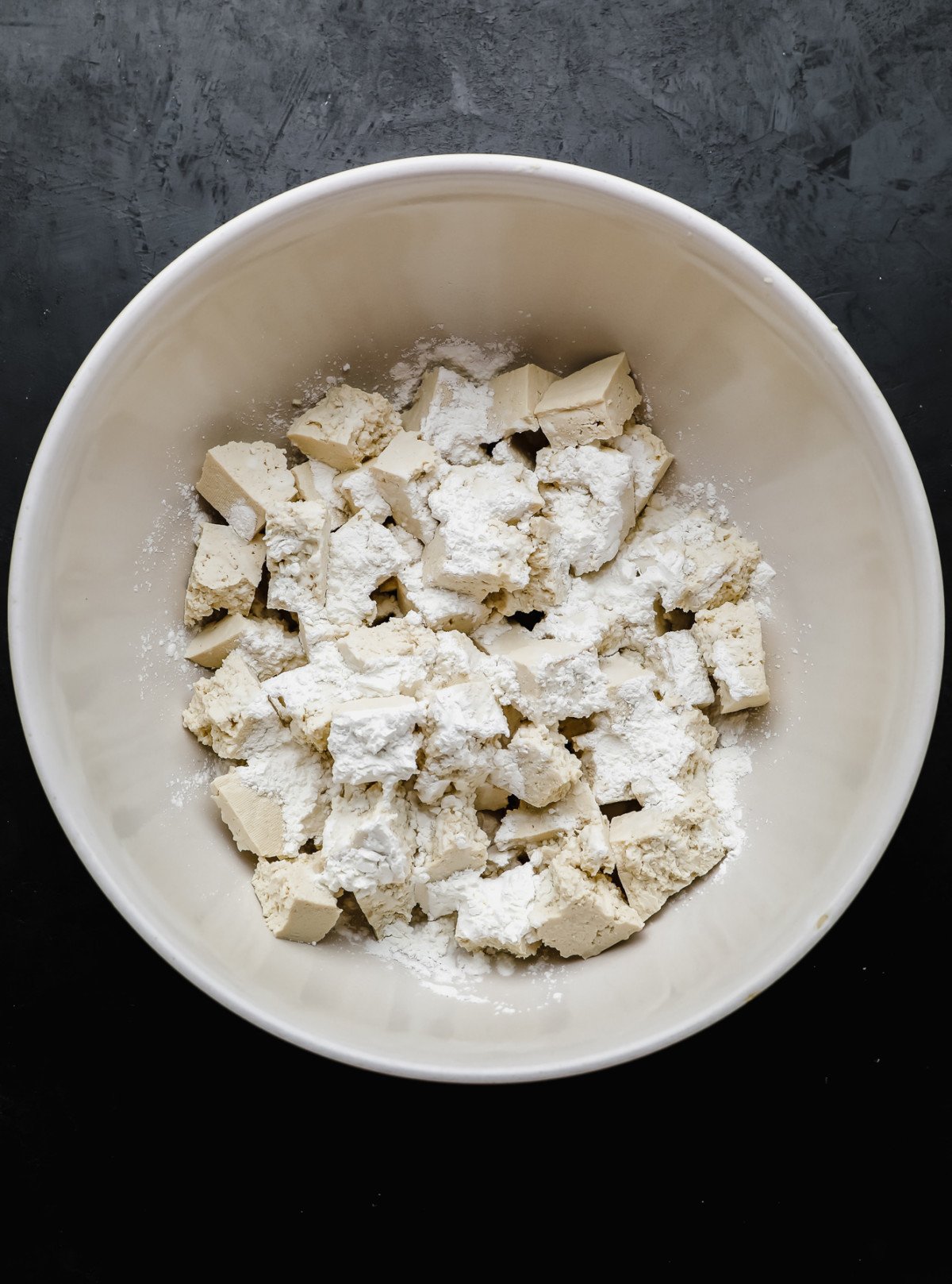 Tofu pieces covered in cornstarch in a large white bowl.