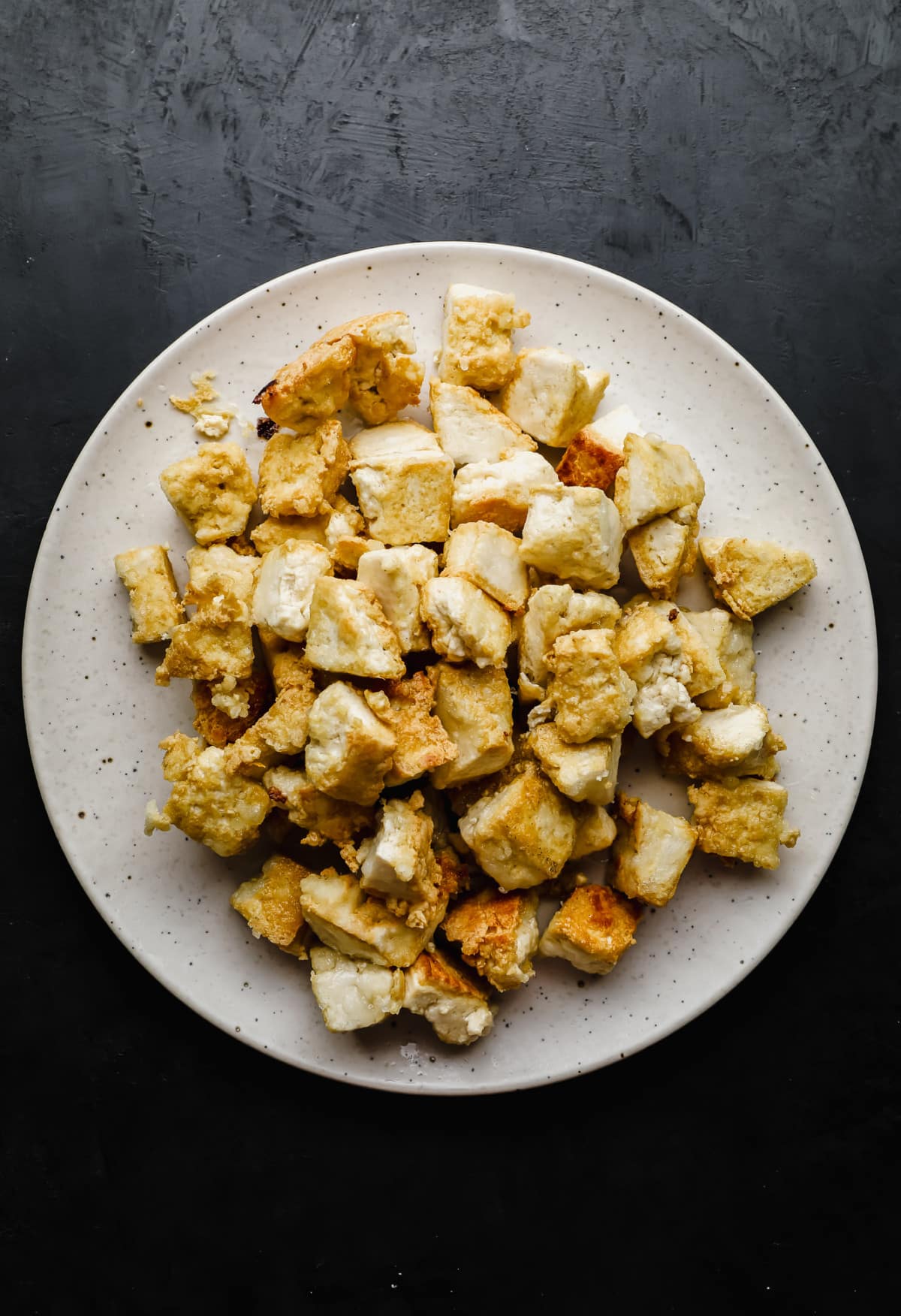a pile of fried tofu pieces on a white plate.