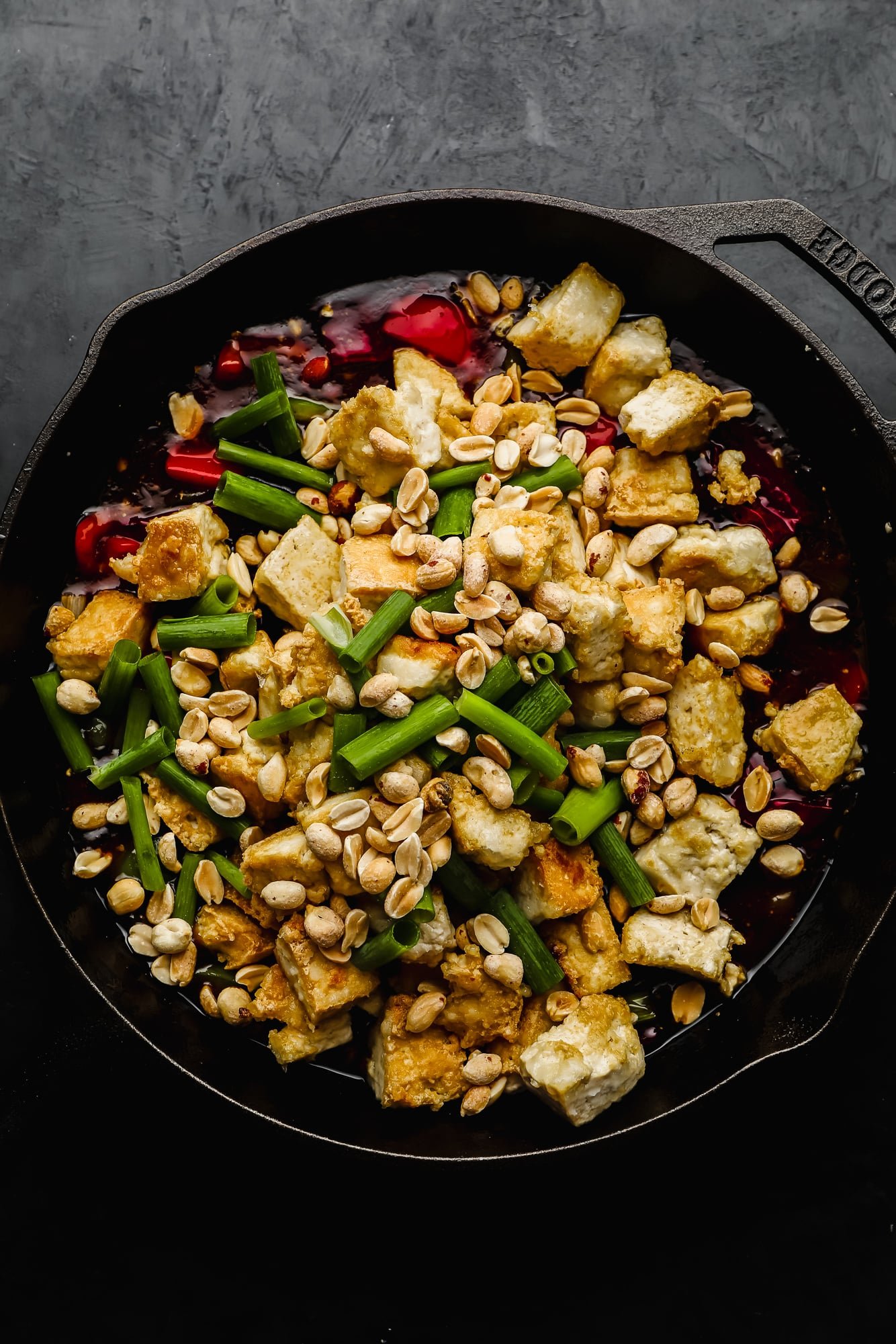 fried tofu pieces, peanuts, and green onions on top of stir fried vegetables in a black cast iron skillet.