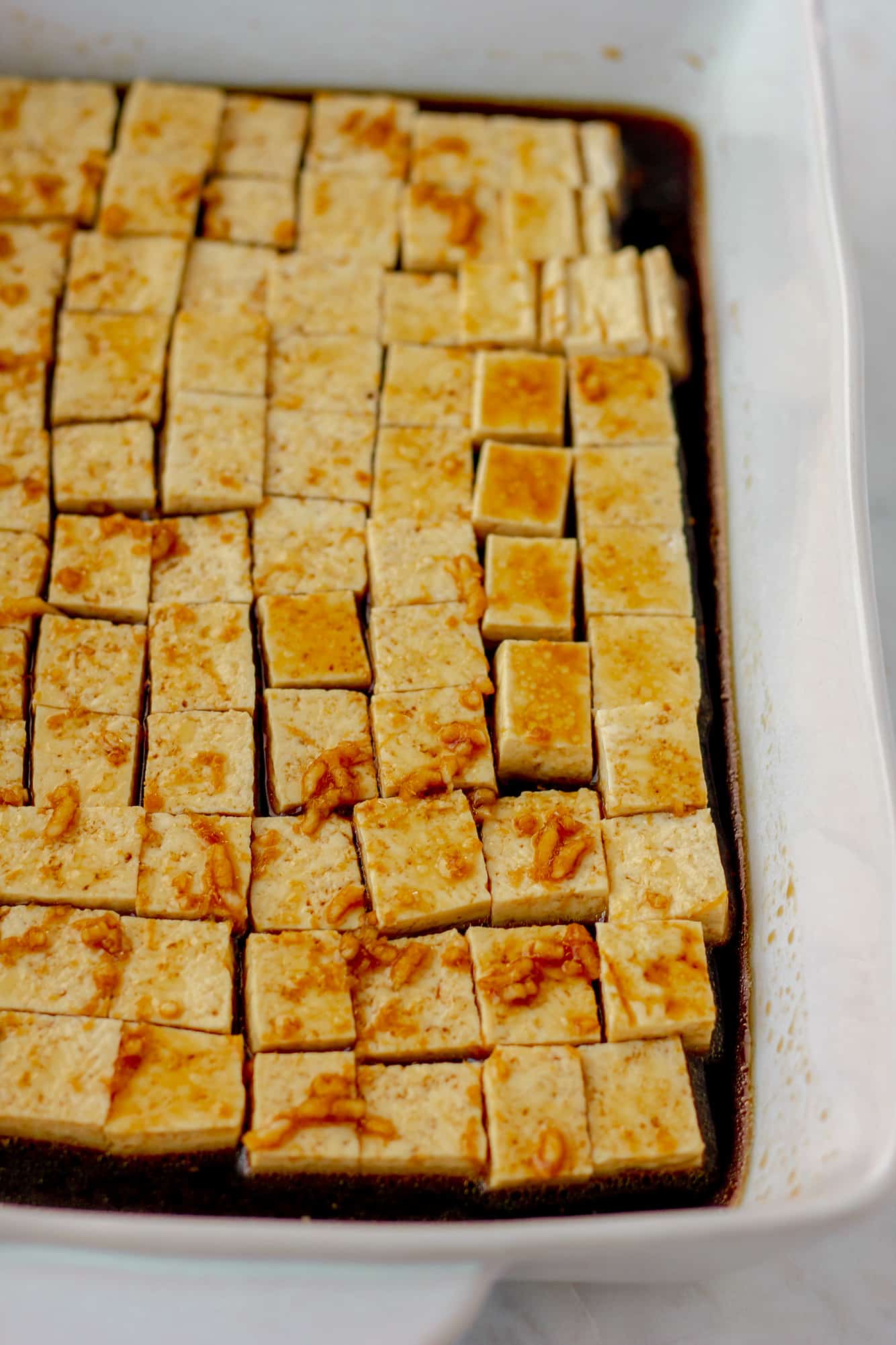 rows of tofu cubes covered in a marinade in a white baking dish.
