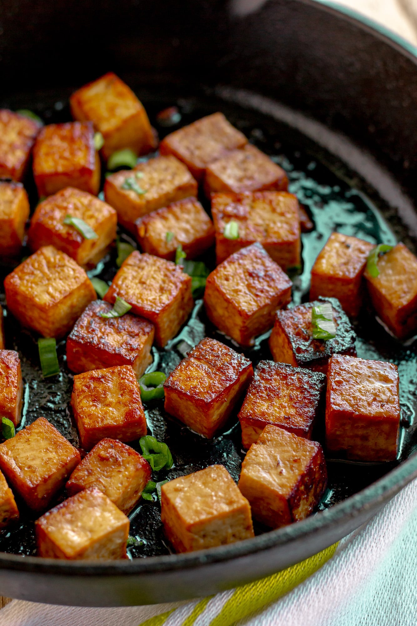 frying marinated tofu cubes in a black skillet.