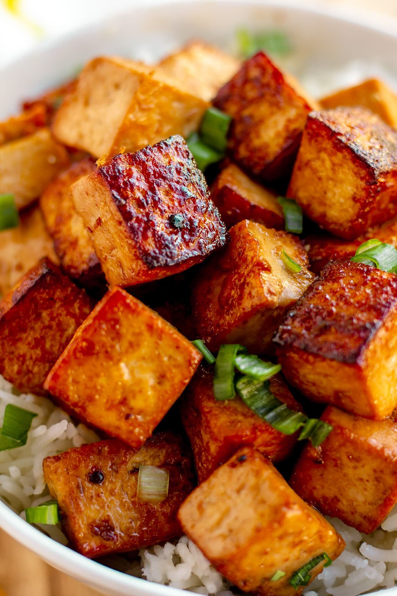 close up on cooked and marinated tofu cubes in a white bowl with rice.