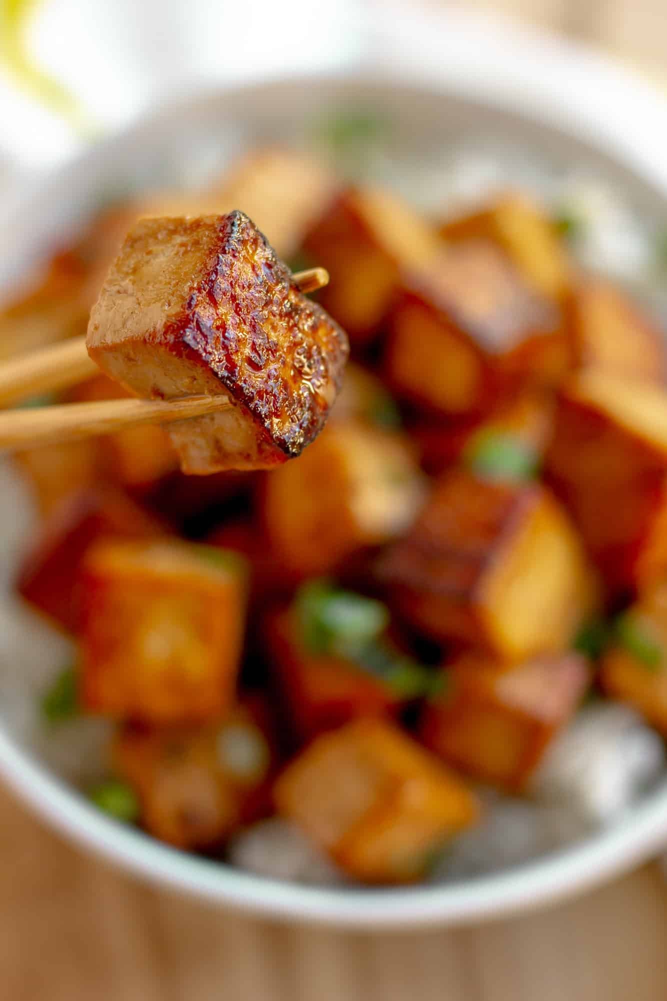 close up on a marinated tofu cube being held up with chopsticks.