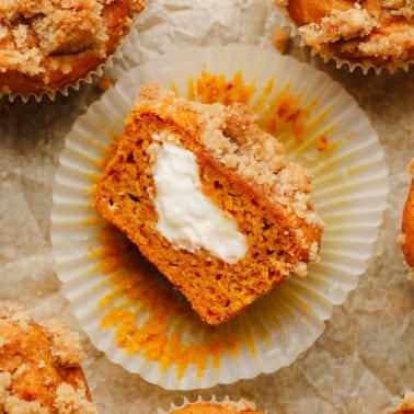 a vegan pumpkin cream cheese muffin sliced in half and turned on its side, showing vegan cream cheese in the middle.