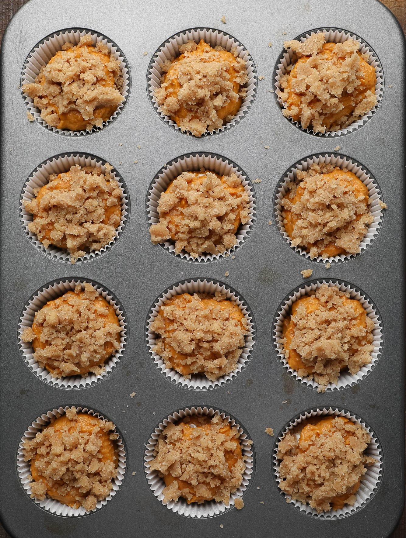 unbaked vegan pumpkin cream cheese muffins topped with cinnamon streusel in a muffin tin.