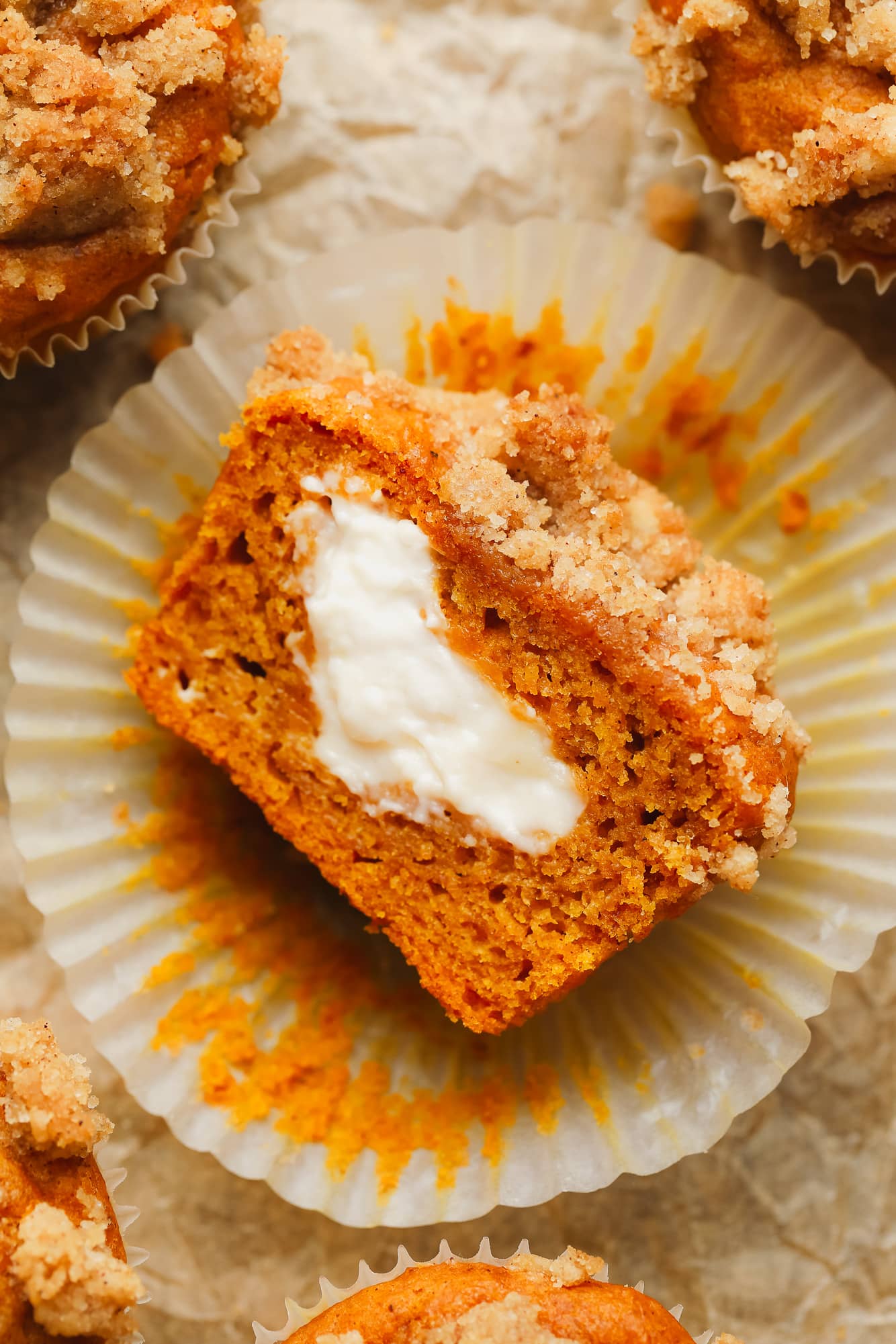 a vegan pumpkin cream cheese muffin sliced in half and turned on its side, showing vegan cream cheese in the middle.