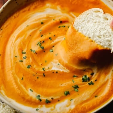 close up of a piece of bread being dipped in a bowl of vegan pumpkin soup.