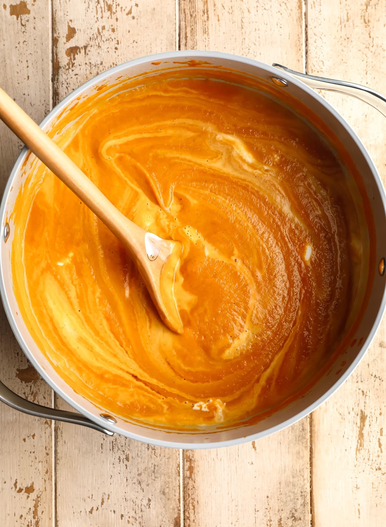 using a wooden spoon to stir pumpkin soup in a large grey pot.