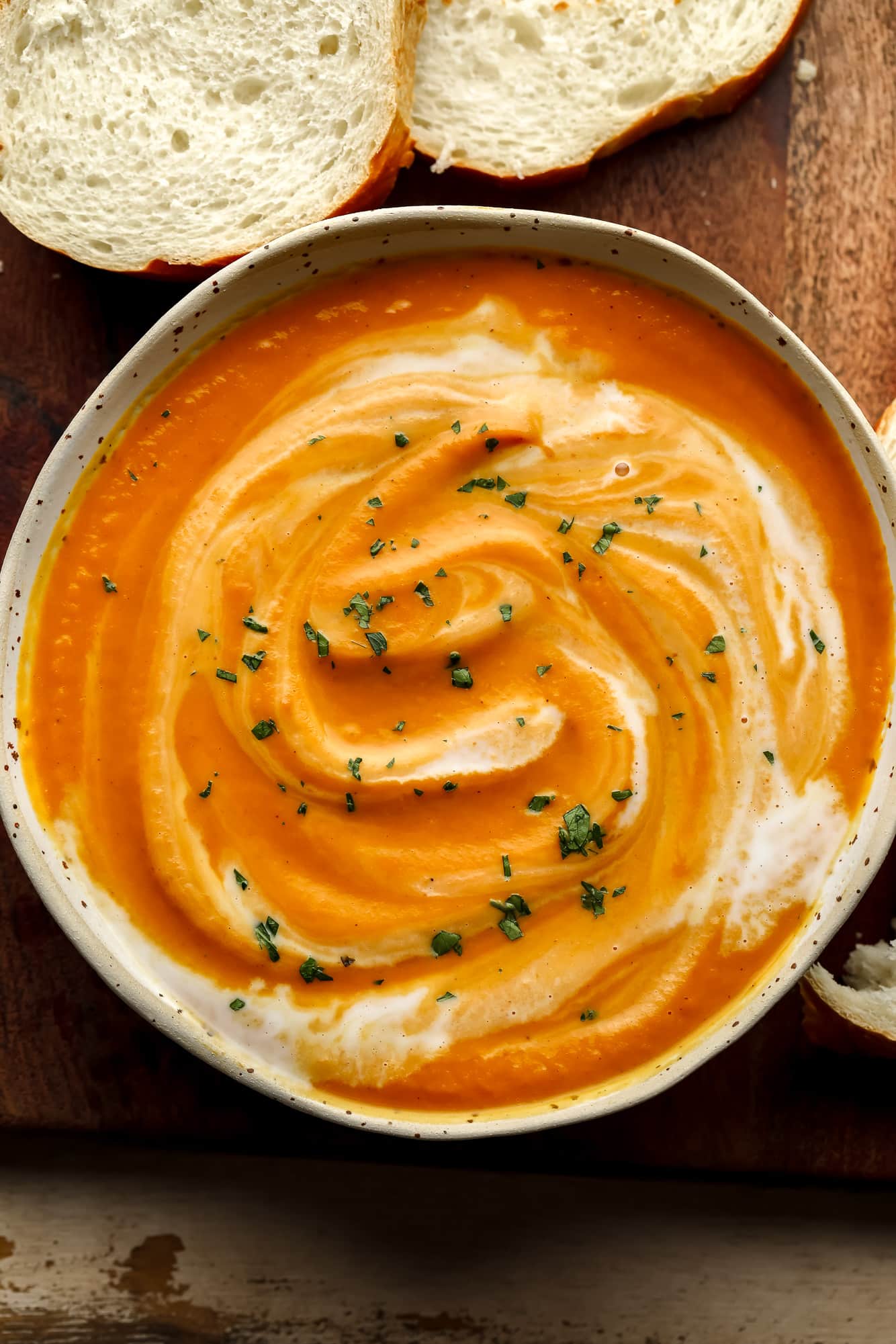 vegan pumpkin soup in a white bowl surrounded by slices of bread.