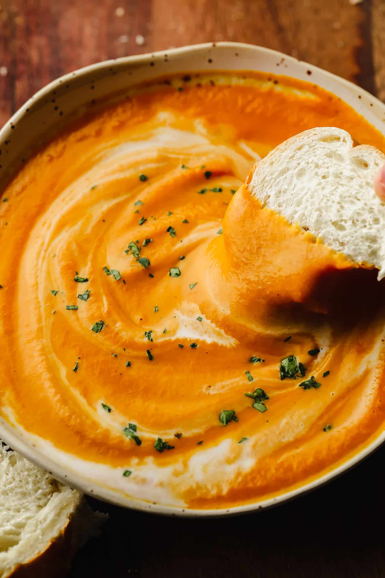 dipping a piece of bread in a bowl of vegan pumpkin soup.