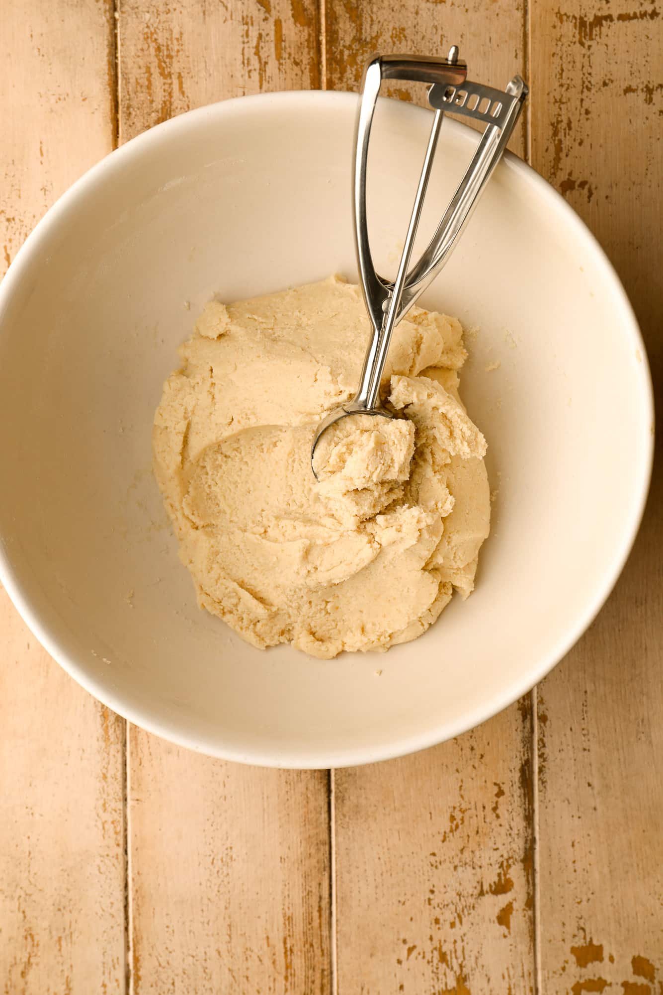 using a cookie scoop to scoop white cookie dough out of a white bowl.