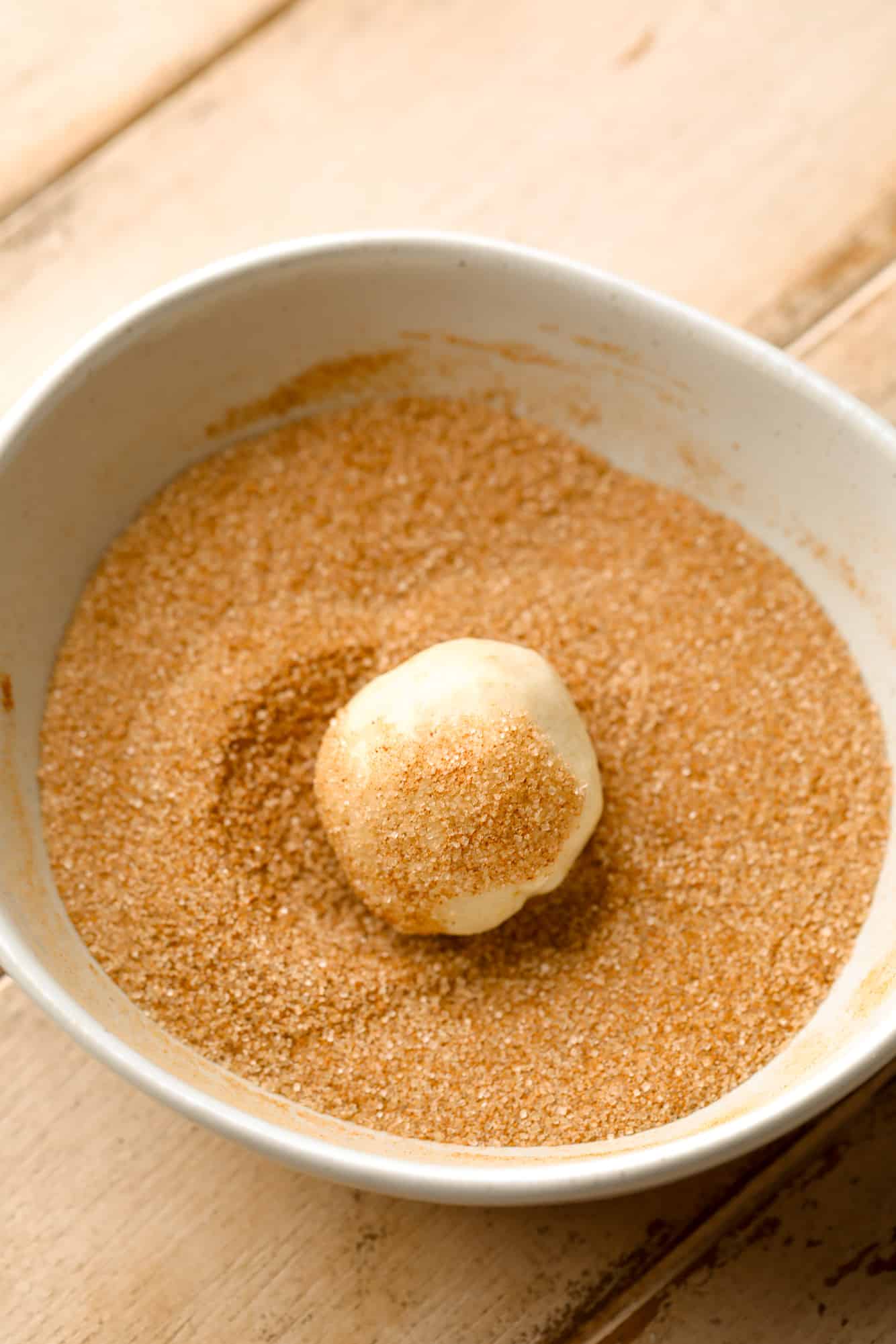 Rolling a cookie dough ball in a bowl of cinnamon sugar.