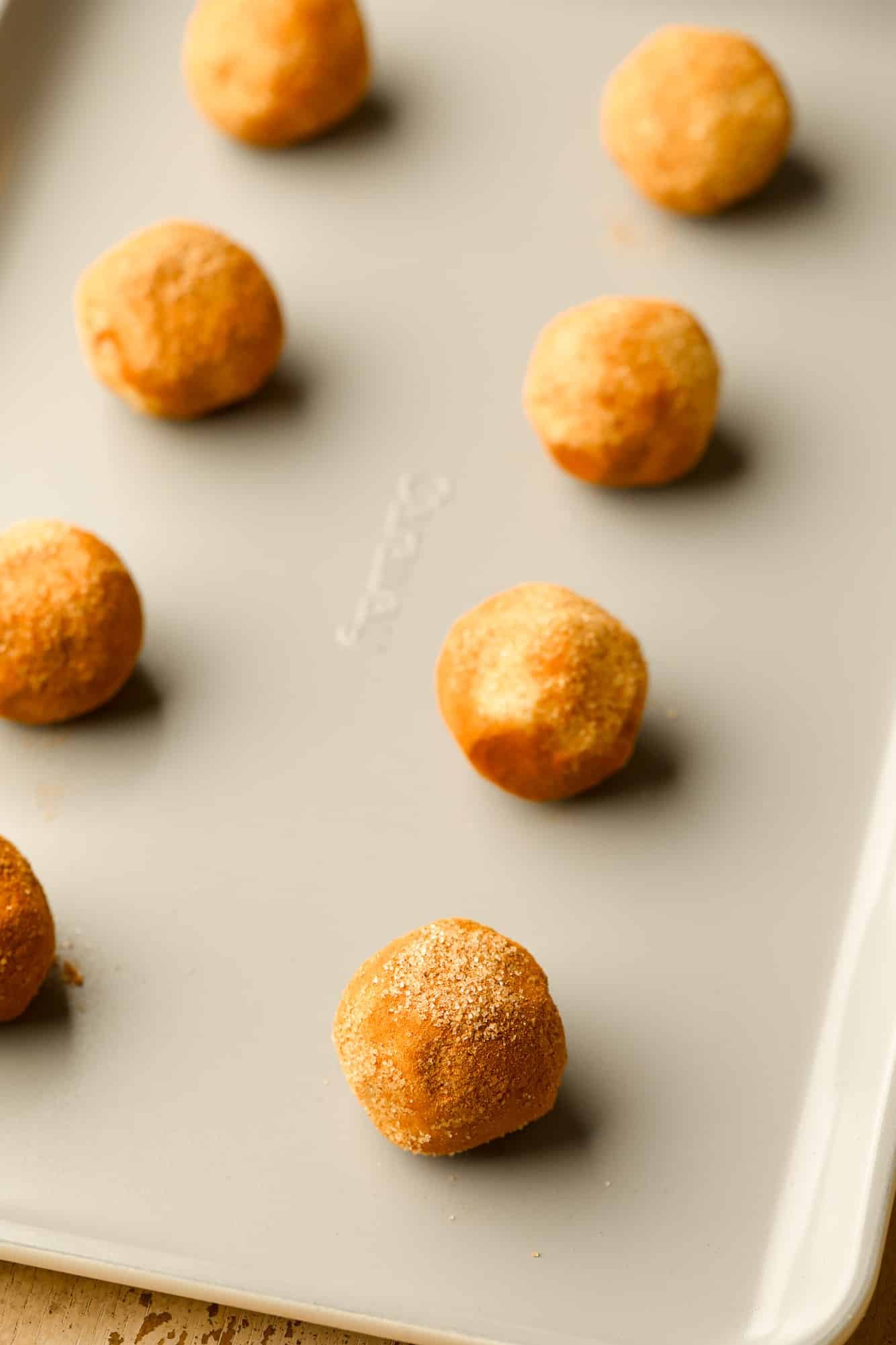 cinnamon sugar-coated cookie dough balls in rows on a metal baking sheet.