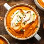 carrot lentil soup topped with vegan yogurt and green herbs in a white soup bowl.