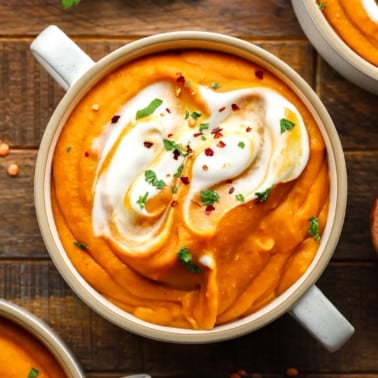 carrot lentil soup topped with vegan yogurt and green herbs in a white soup bowl.