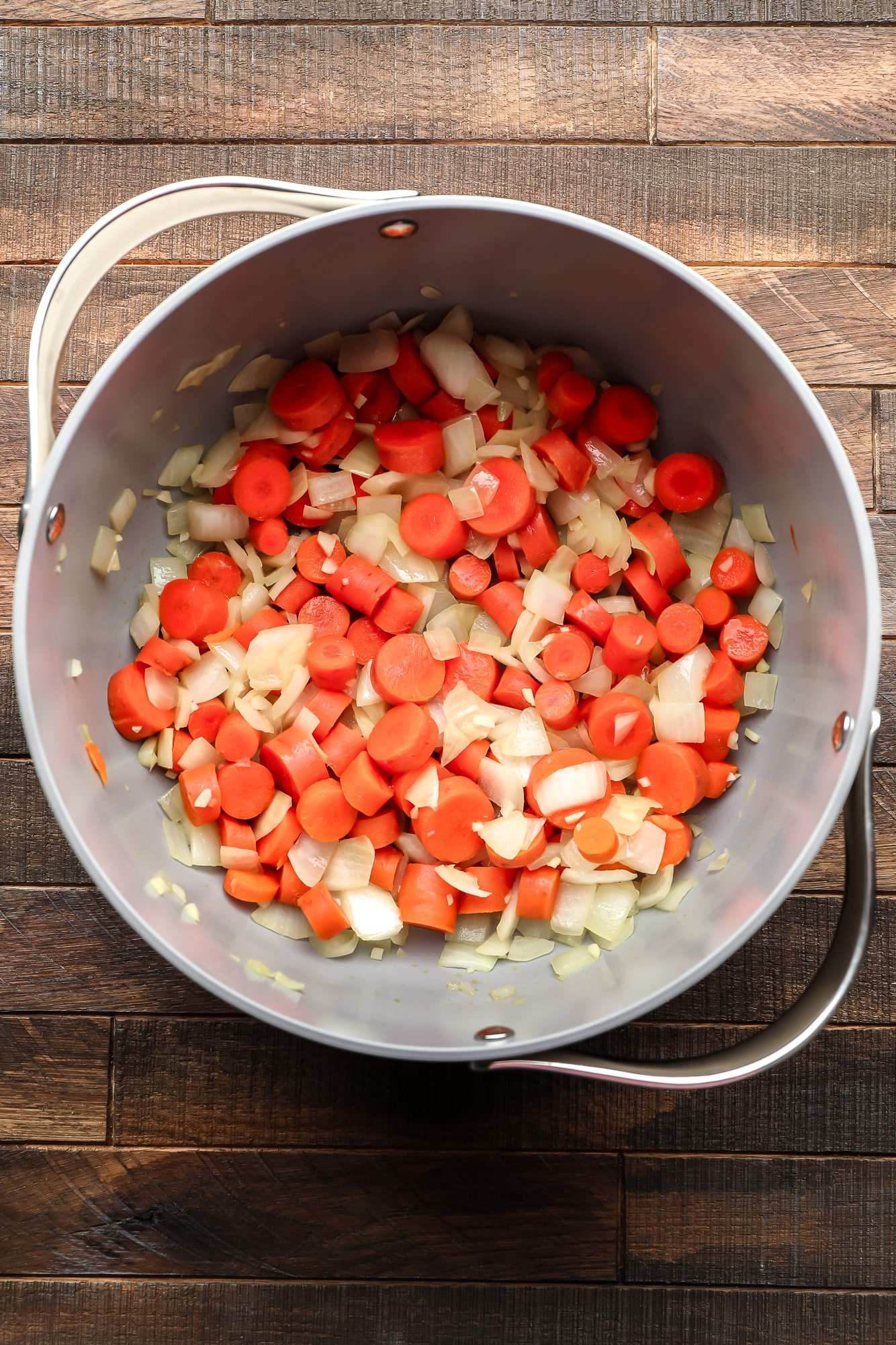 cooking chopped carrots, onions, and garlic in a large grey pot.