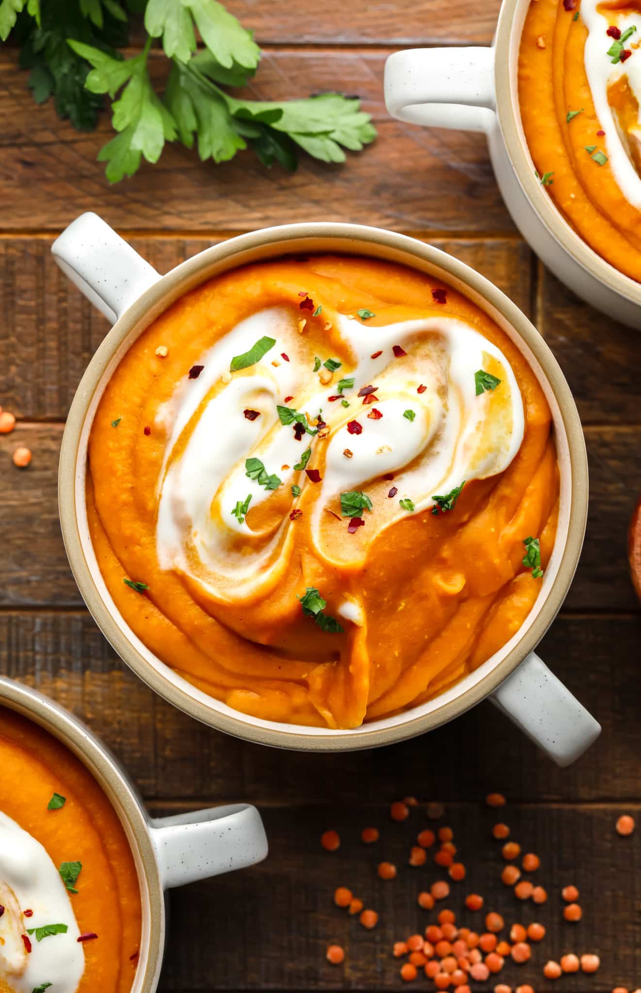 carrot lentil soup topped with vegan yogurt and green herbs in a white soup bowl.