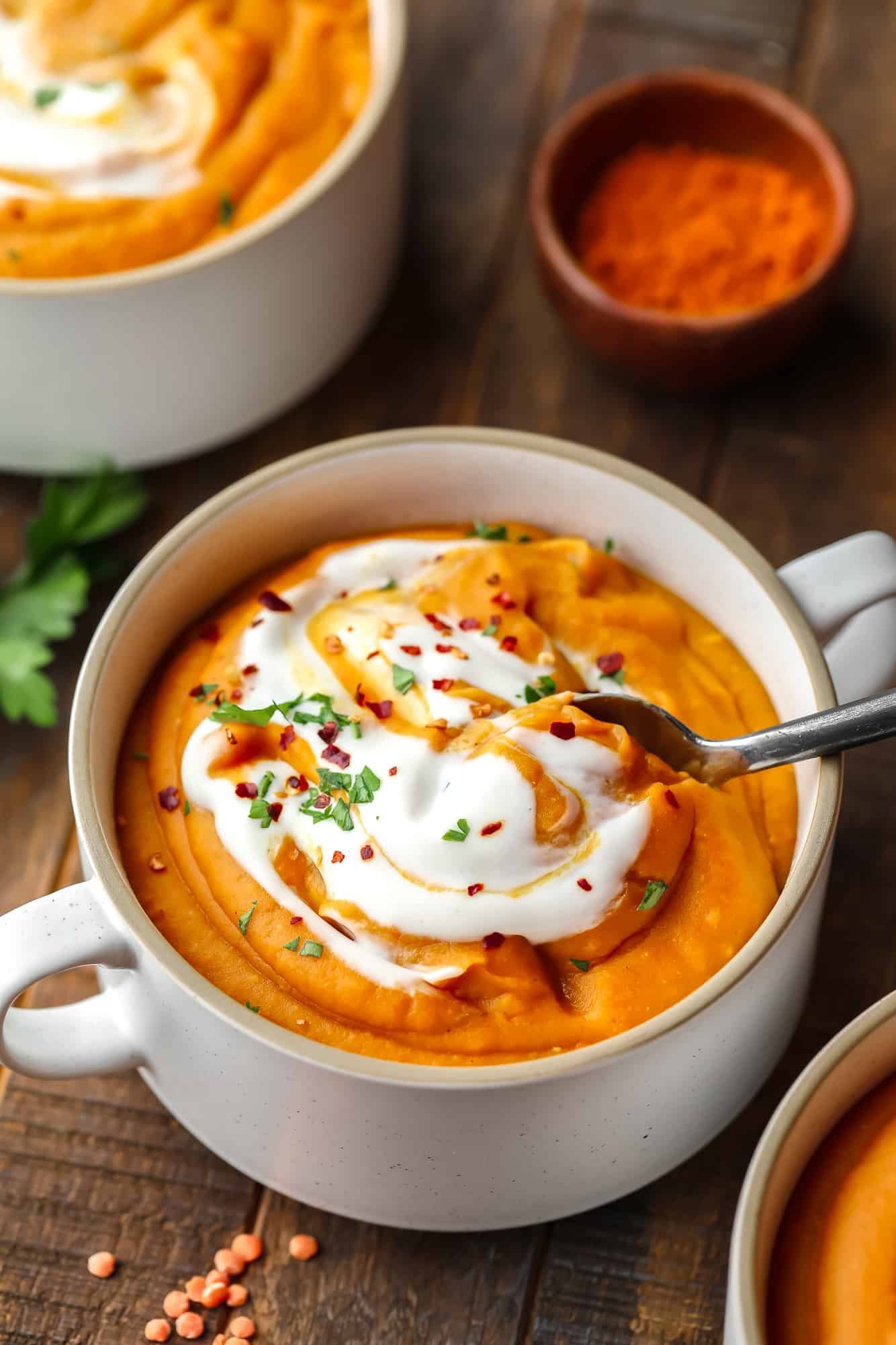 Nehmen Sie mit einem Metalllöffel eine Kugel Karotten-Linsen-Suppe aus einer weißen Suppenschüssel.