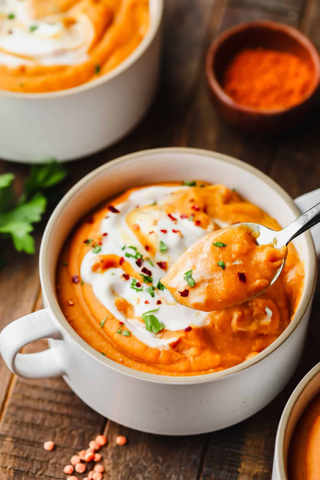 using a metal spoon to lift a scoop of carrot lentil soup from a white soup bowl.