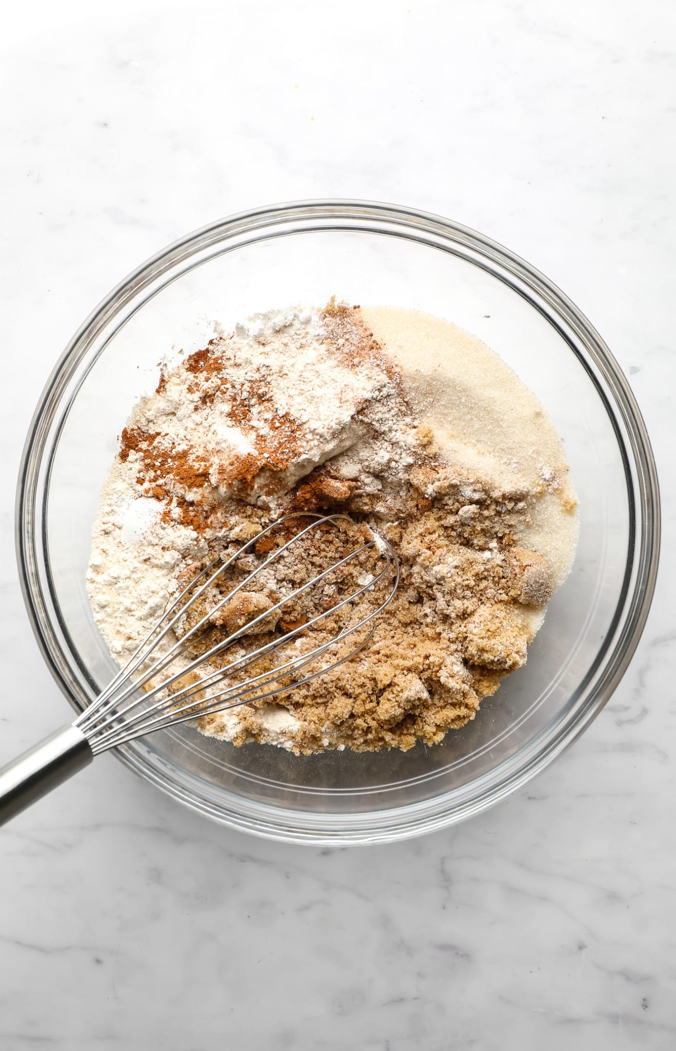 whisking the dry ingredients for vegan apple muffins together in a glass bowl.